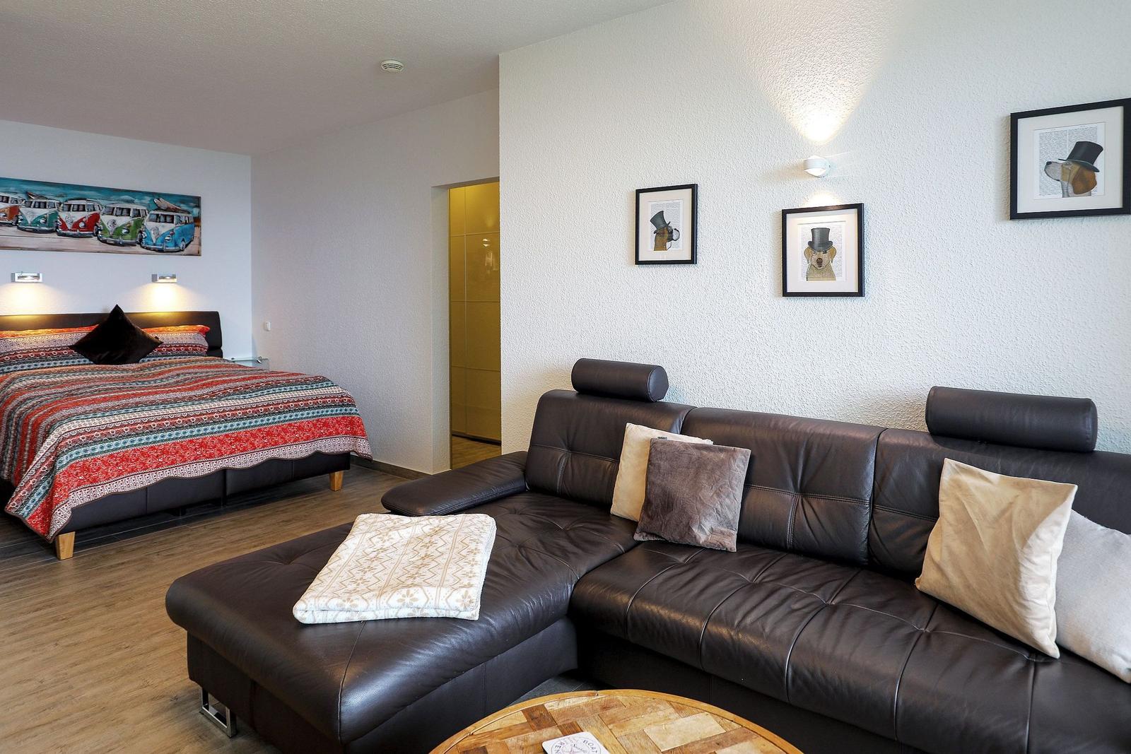 Wohnzimmer mit Ledersofa und Schlafzimmer mit Bett und Wandbild.
