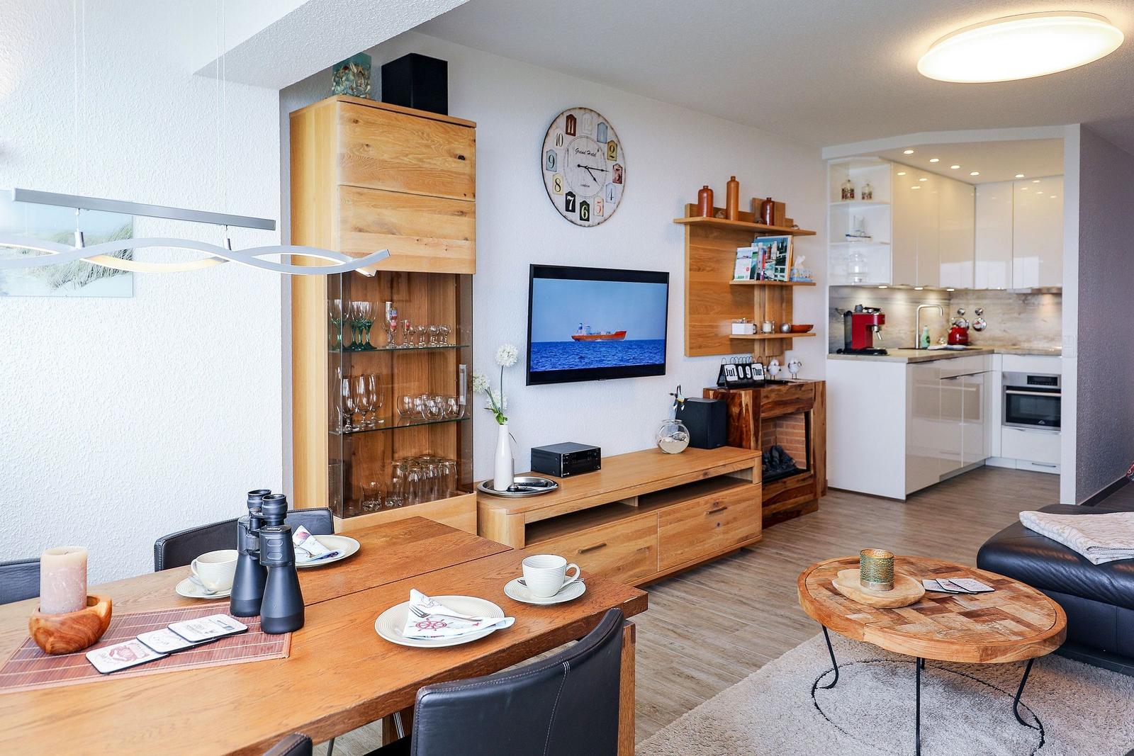 Wohnzimmer mit Esstisch, TV und Küche im Hintergrund.