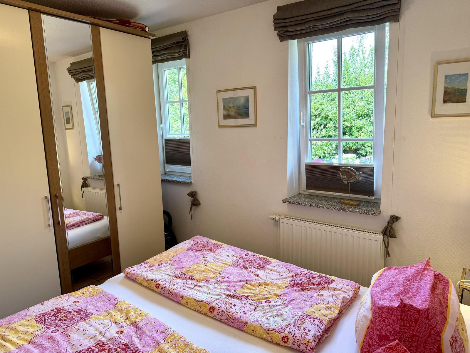 Schlafzimmer mit Doppelbett, Kleiderschrank und Fenster mit Blick auf Grün.