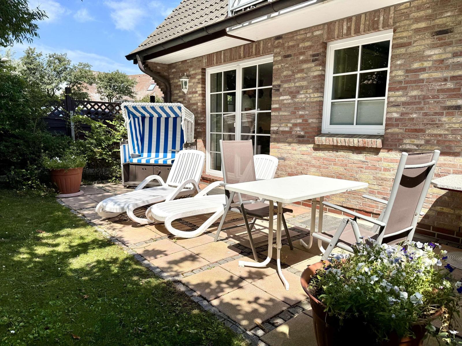 Terrasse mit Liegestühlen, Tisch und blau-weißem Strandkorb vor Backsteinhaus.