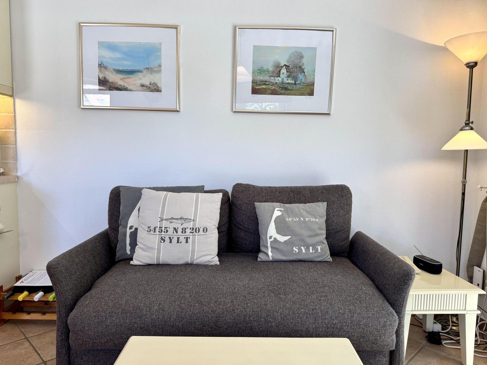 Grauer Sofa mit Kissen, Wandbilder und Stehlampe im Wohnbereich.