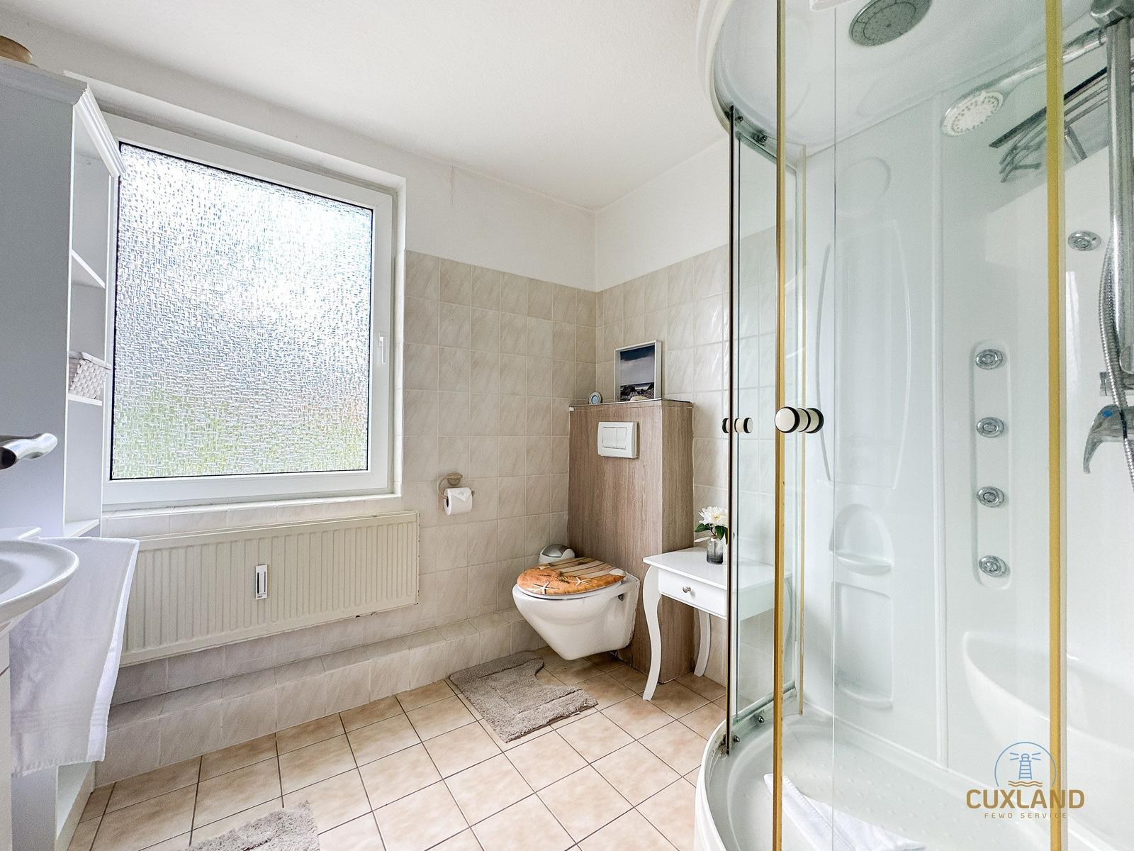 Badezimmer mit Dusche, Toilette und Waschbecken. Fenster mit getöntem Glas.
