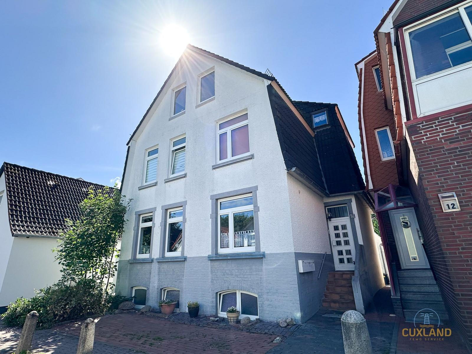Weißes Haus mit dunklem Dach und Fenstern. Eingang mit Stufen. Sonniger Tag.