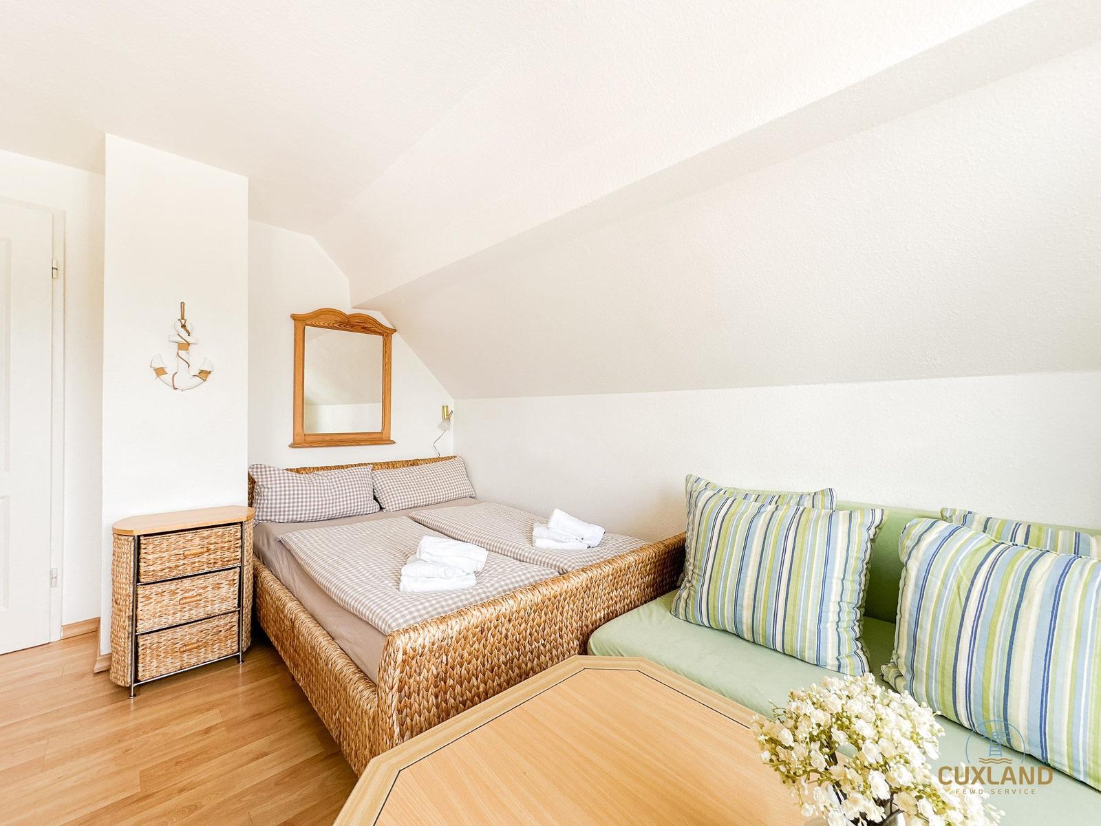Schlafzimmer mit Doppelbett, Sofa und Schrank unter schrägem Dach