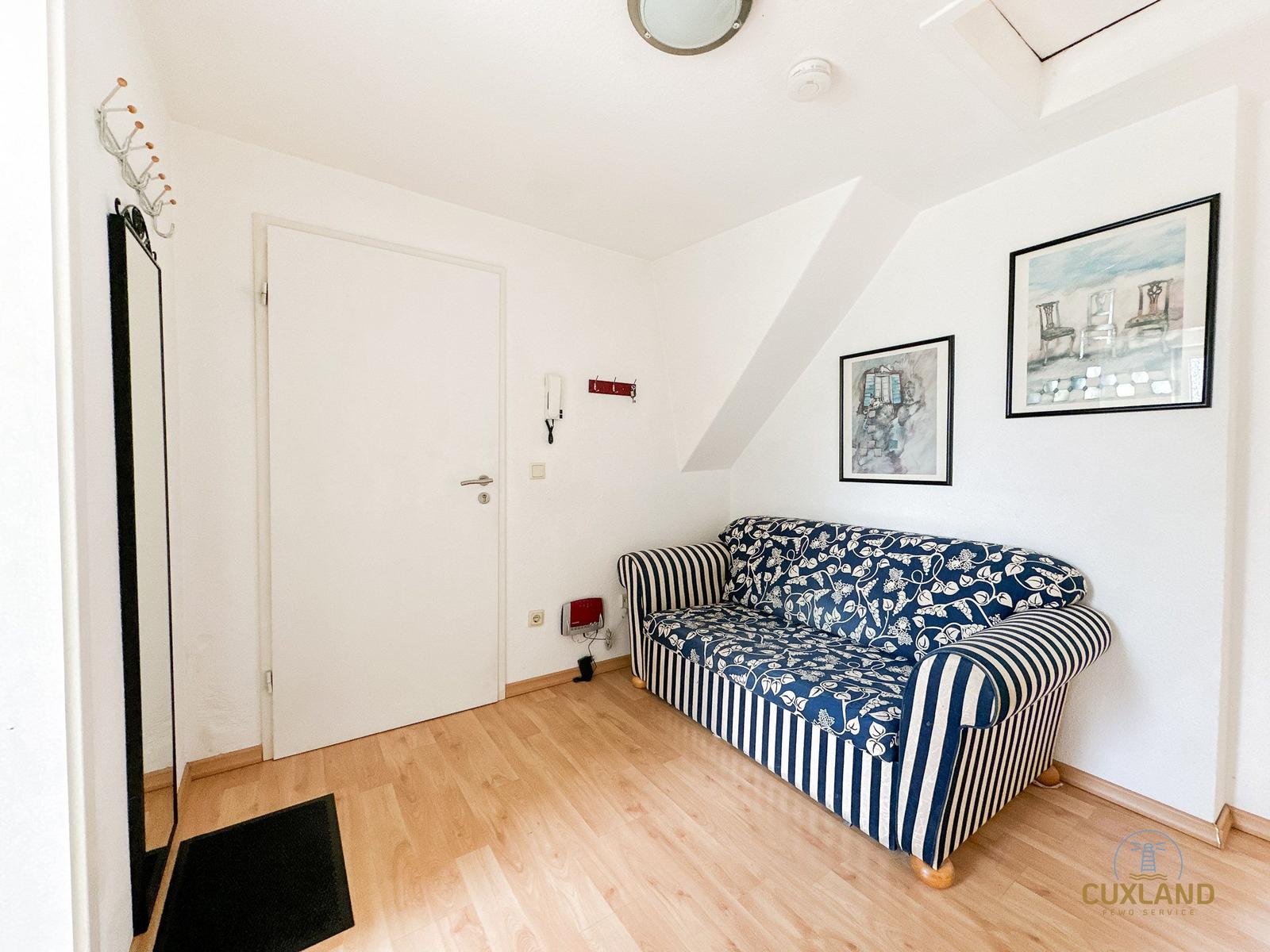 Ein Raum mit Sofa, Wandbildern und Holzboden. Tür und Spiegel sind sichtbar.