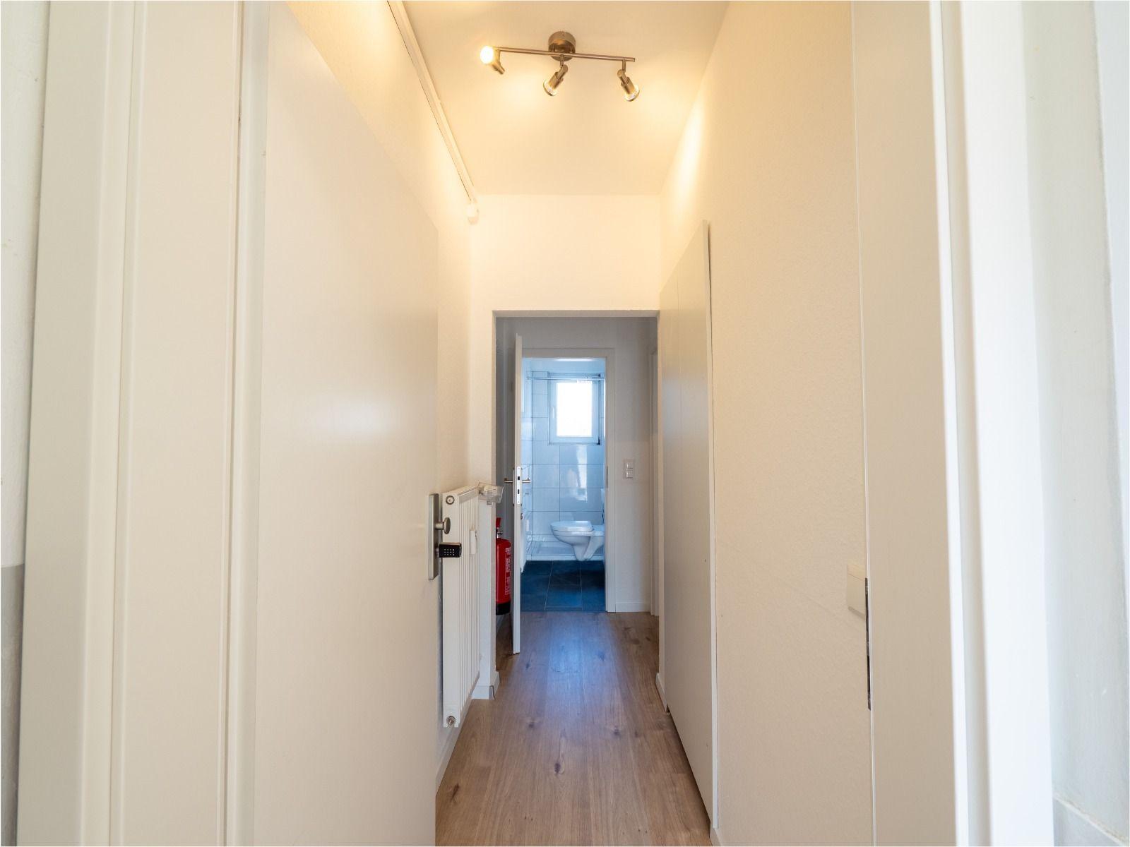 Flur mit Holzboden und Tür zum Bad mit Toilette