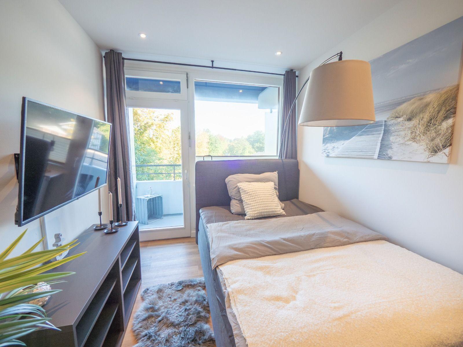 Schlafzimmer mit Bett, Fernseher und Balkonzugang.