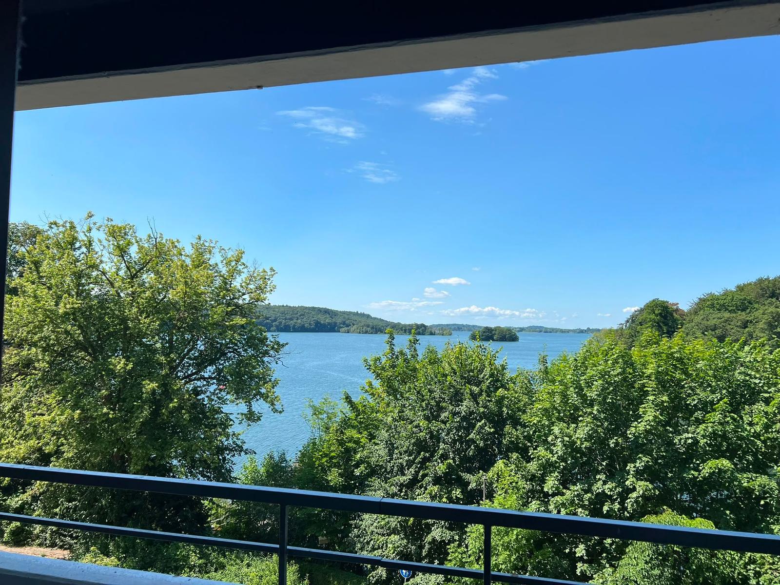 Blick vom Balkon auf einen See mit Bäumen und Inseln unter blauem Himmel.