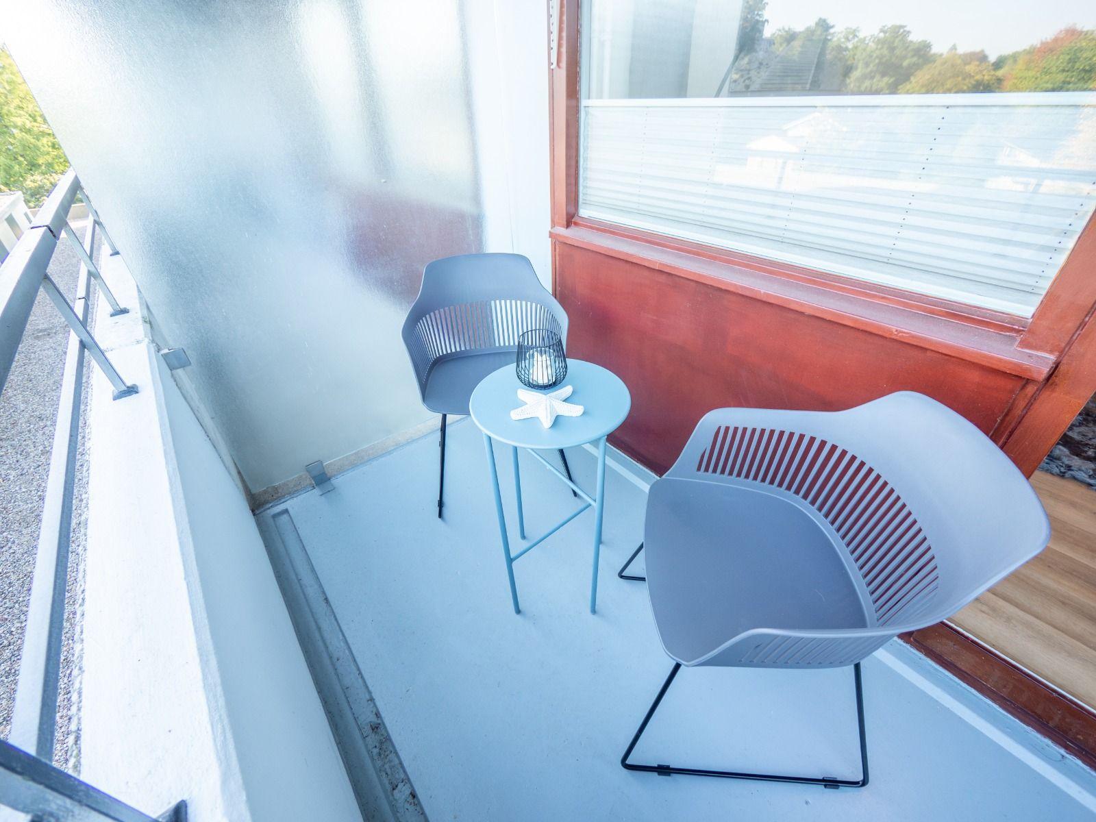 Balkon mit zwei grauen Stühlen und einem blauen Tisch mit Laterne und Seestern.