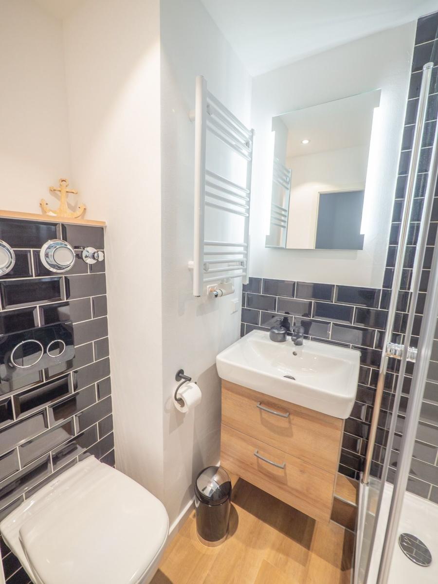 Badezimmer mit Dusche, Waschbecken und Toilette. Schwarze Fliesen und Holzoptik.