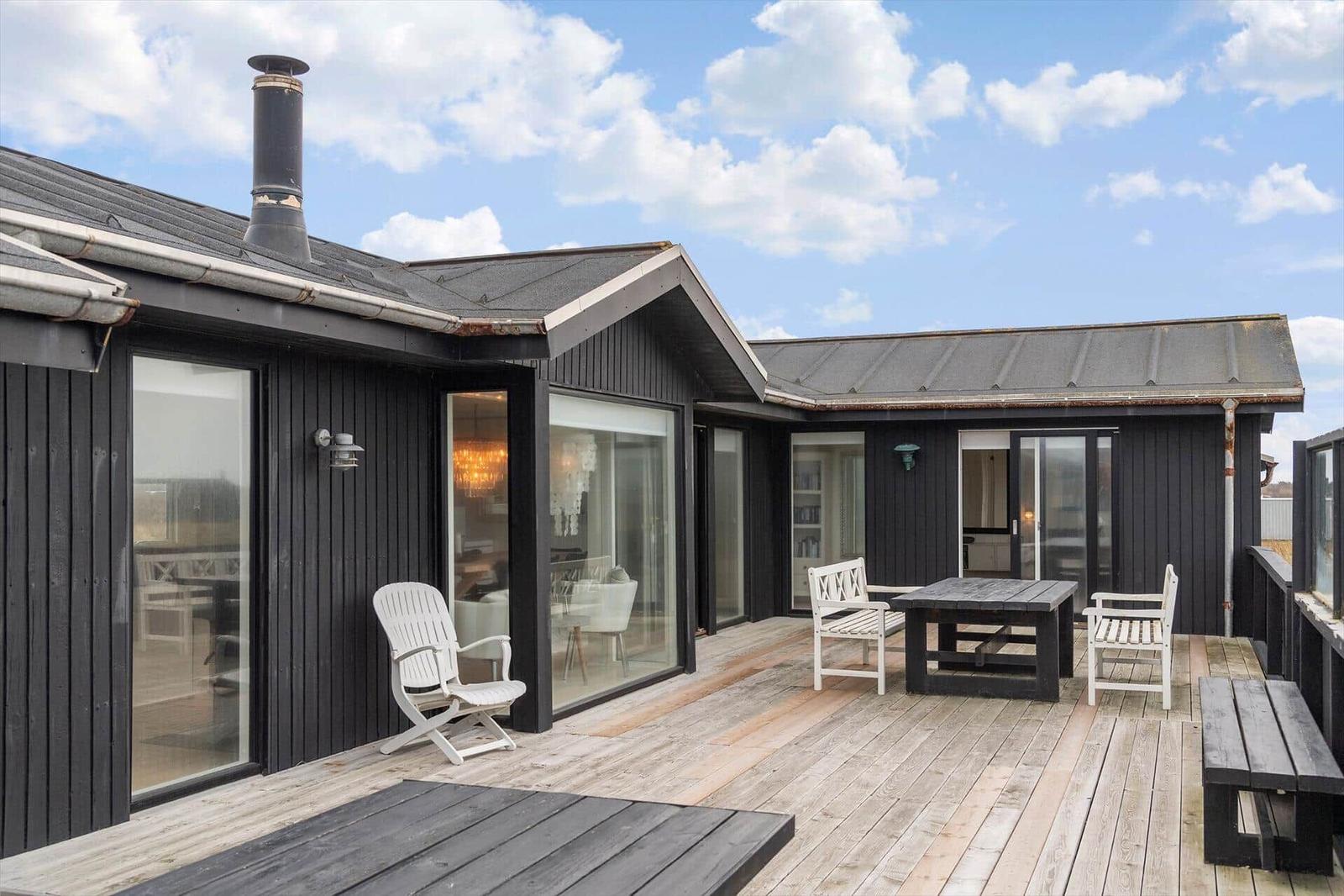 Terrasse mit Tisch, Stühlen und Blick in das Haus. Schwarze Fassade und Holzdecke.