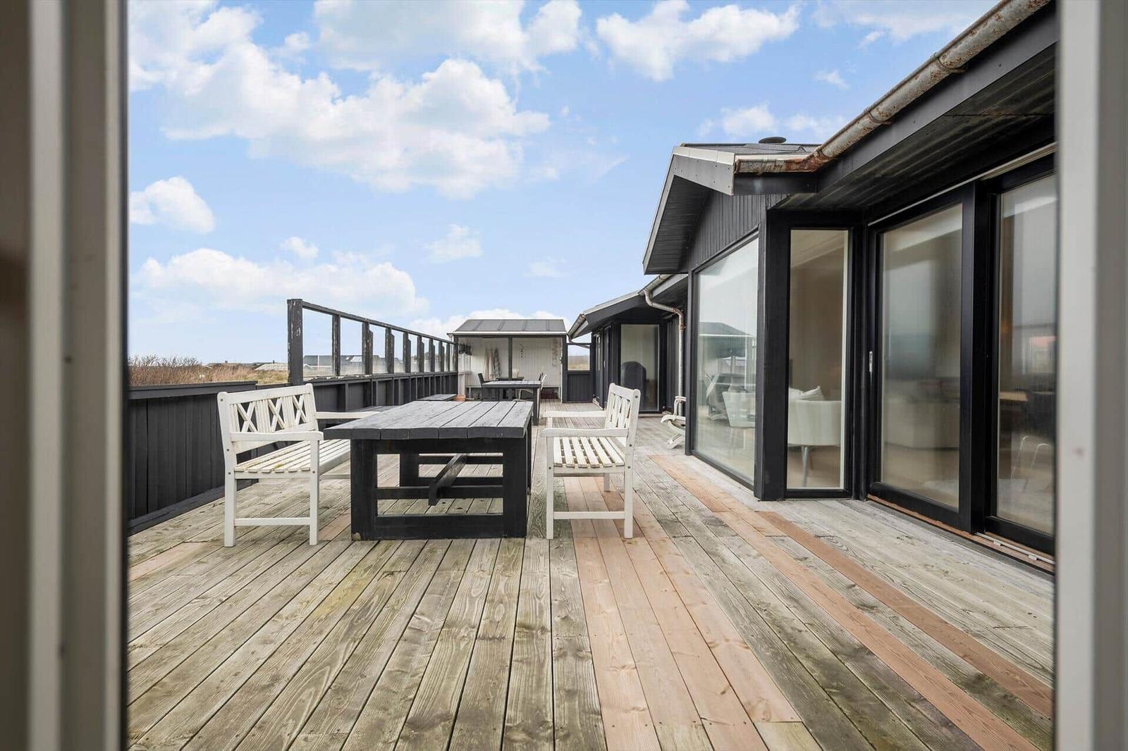Terrasse mit Tisch und Stühlen, Holzboden und Blick auf das Gelände.