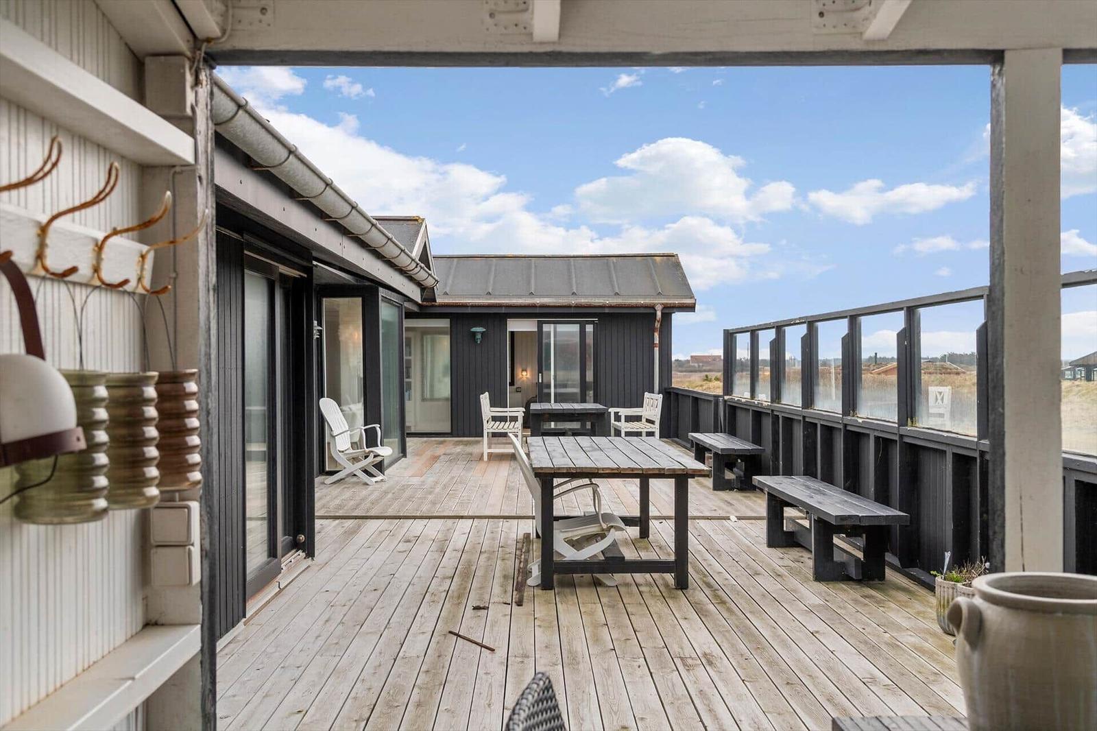 Terrasse mit Tisch, Bänken und Sitzgelegenheiten. Blick auf Haus und Himmel.
