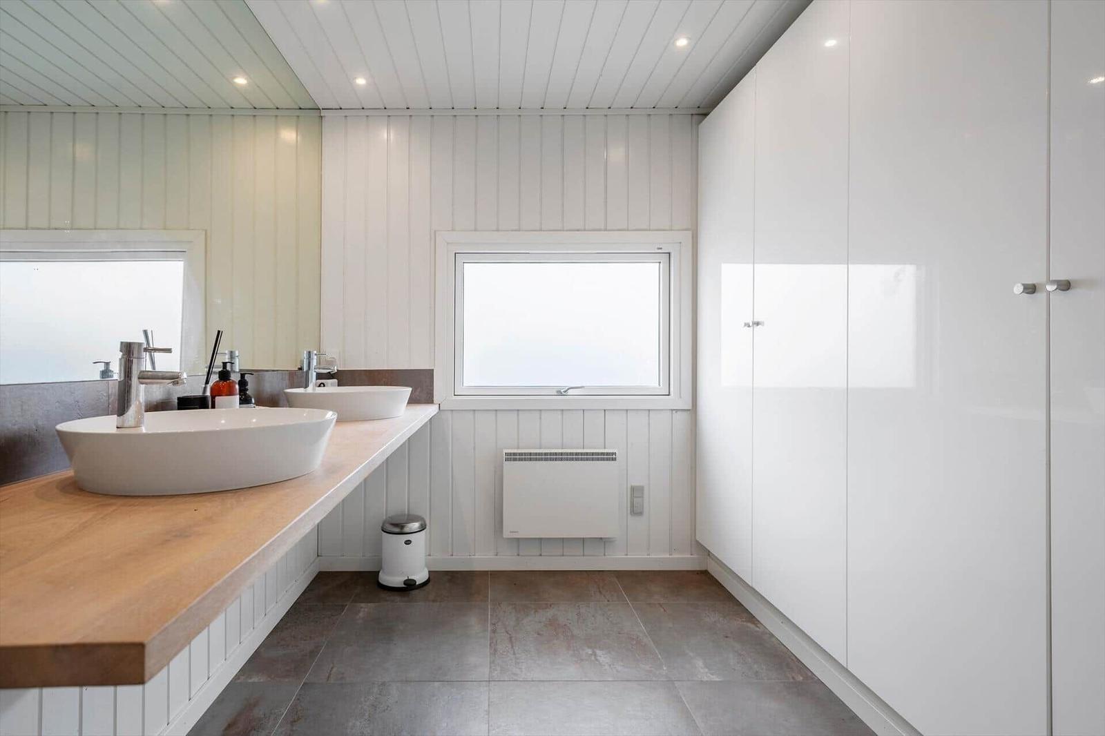 Badezimmer mit zwei Waschbecken, Holzunterlage und großen weißen Schränken.