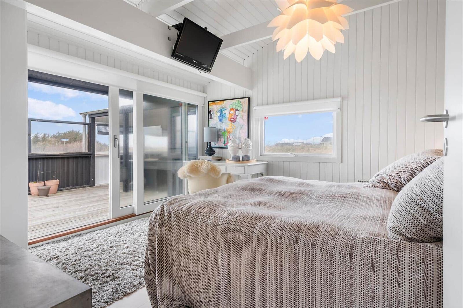 Schlafzimmer mit Bett, Glasfront und Wandbild. Decke mit Lampe und TV.