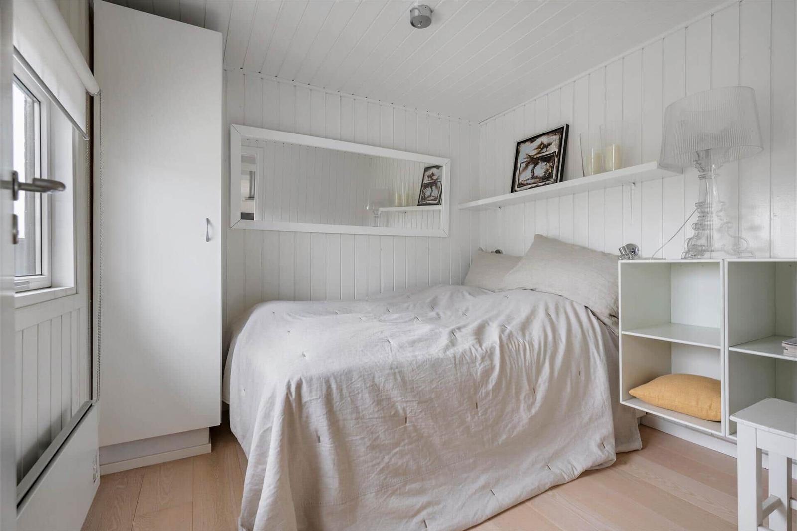 Schlafzimmer mit weißem Bett, Kleiderschrank und Regal. Wandverkleidung und Holzboden.