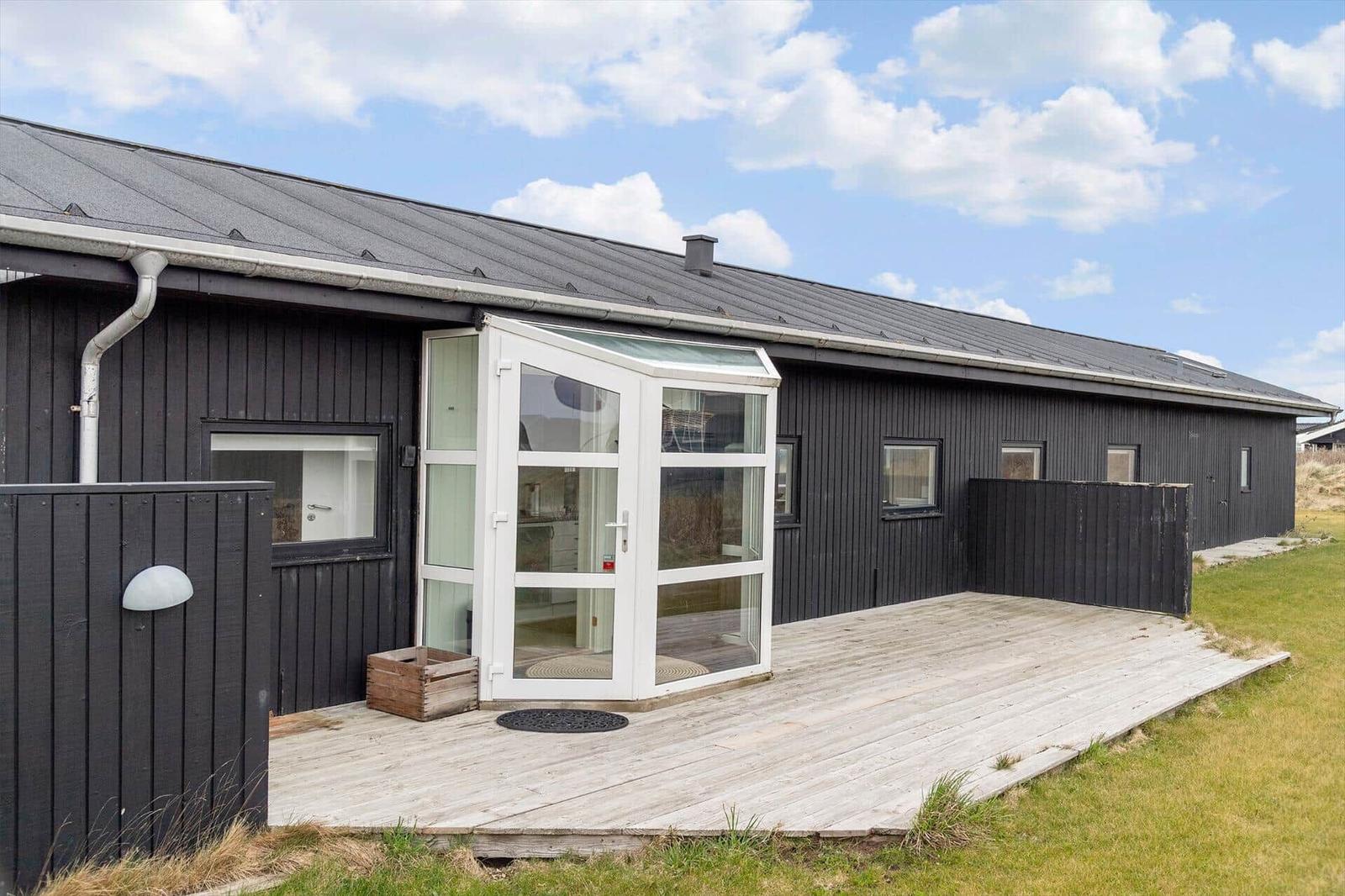 Schwarzes Holzhaus mit weißen Fenstern und Holzterrasse unter blauem Himmel.