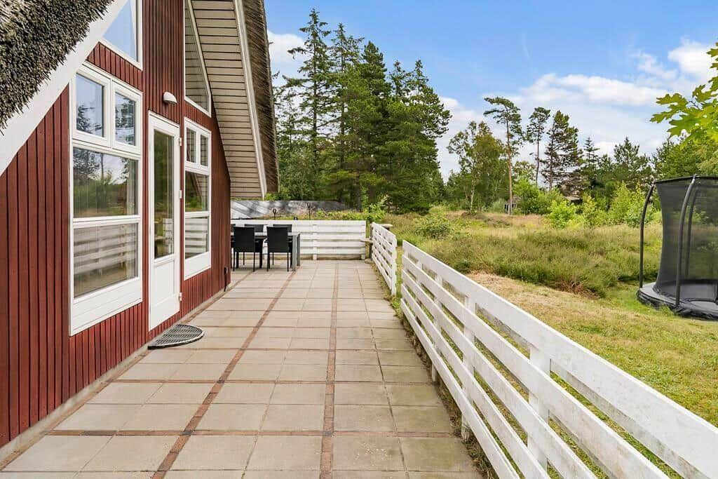 Terrasse mit Tisch, Stühlen und weißem Zaun. Hinterhof mit Trampolin und Wald.
