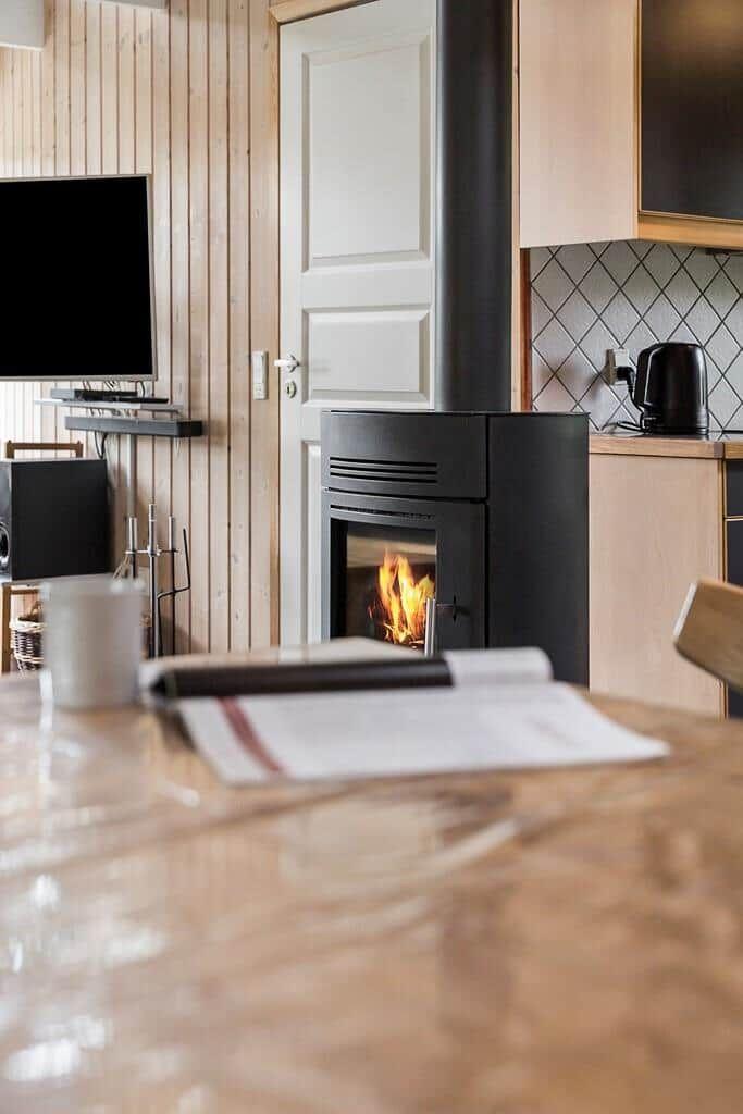 Kamin mit brennendem Feuer, Küchenbereich und Fernseher in einem Holzhaus.