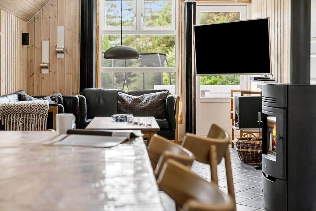 Wohnbereich mit Sofa, Fernseher und Kaminofen. Holzwände und großes Fenster.