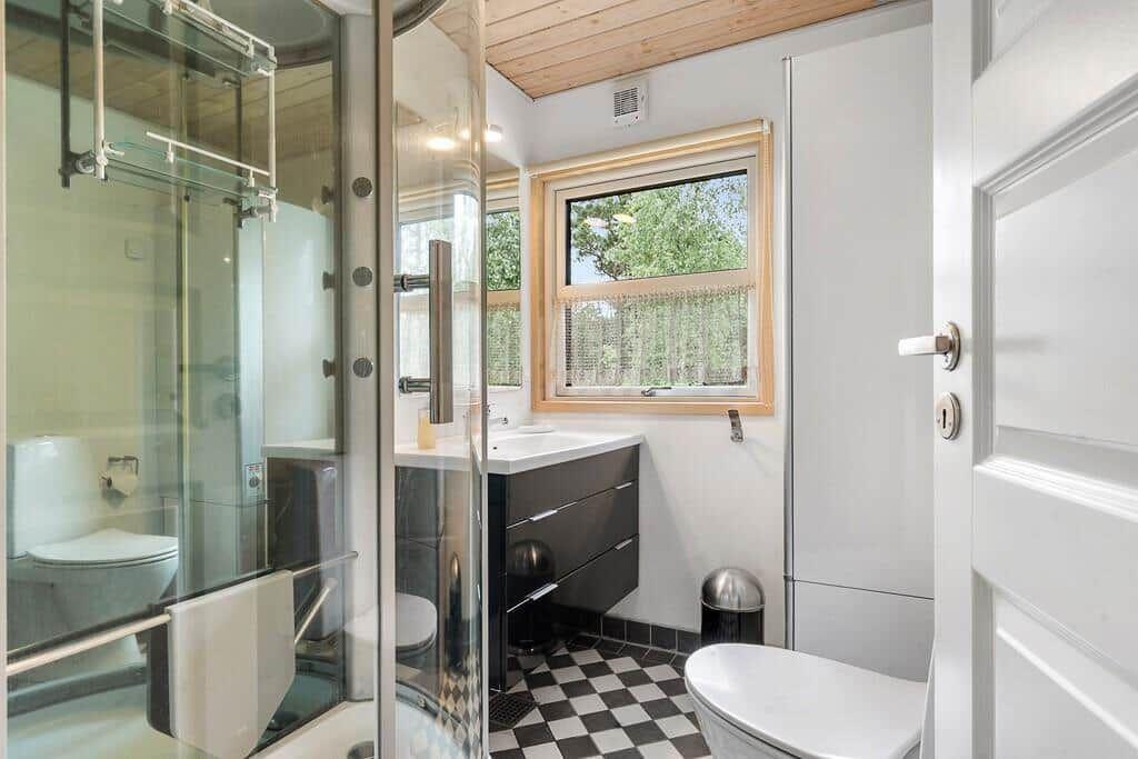 Badezimmer mit Dusche, Waschbecken und Toilette. Schwarze Fliesen und Holzdecke.