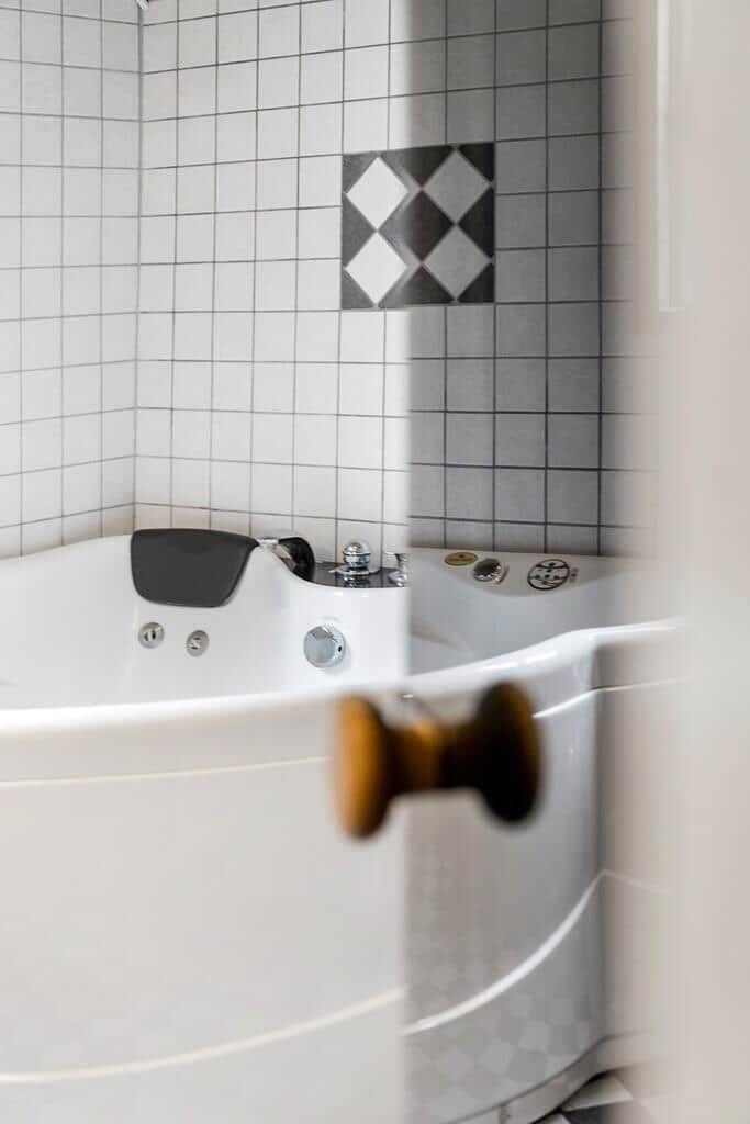 Bad mit Whirlpool und Fliesen in Weiß und Grau mit einem Musterfeld.