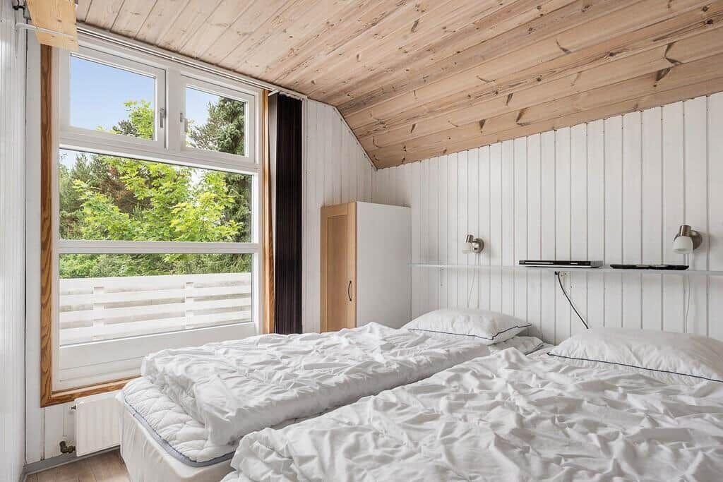 Zwei Betten unter einem Holzdach mit Blick auf grüne Bäume durch ein Fenster.