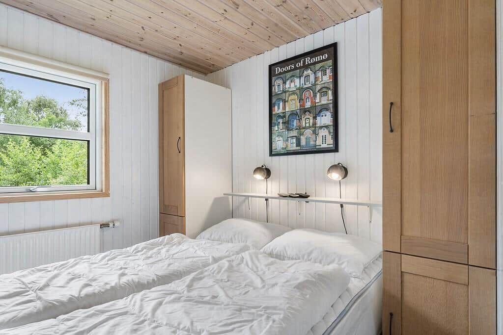 Schlafzimmer mit Doppelbett, Fenster und Holzwand. Wandbild und Nachttische.