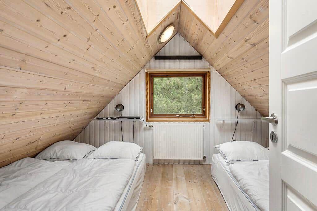 Zimmer mit zwei Betten, Holzwand und Fenster mit Blick auf Bäume.