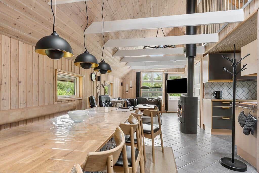 Großes Esszimmer mit Holztisch, Stühlen und moderner Beleuchtung. Küche und Wohnbereich sind sichtbar.