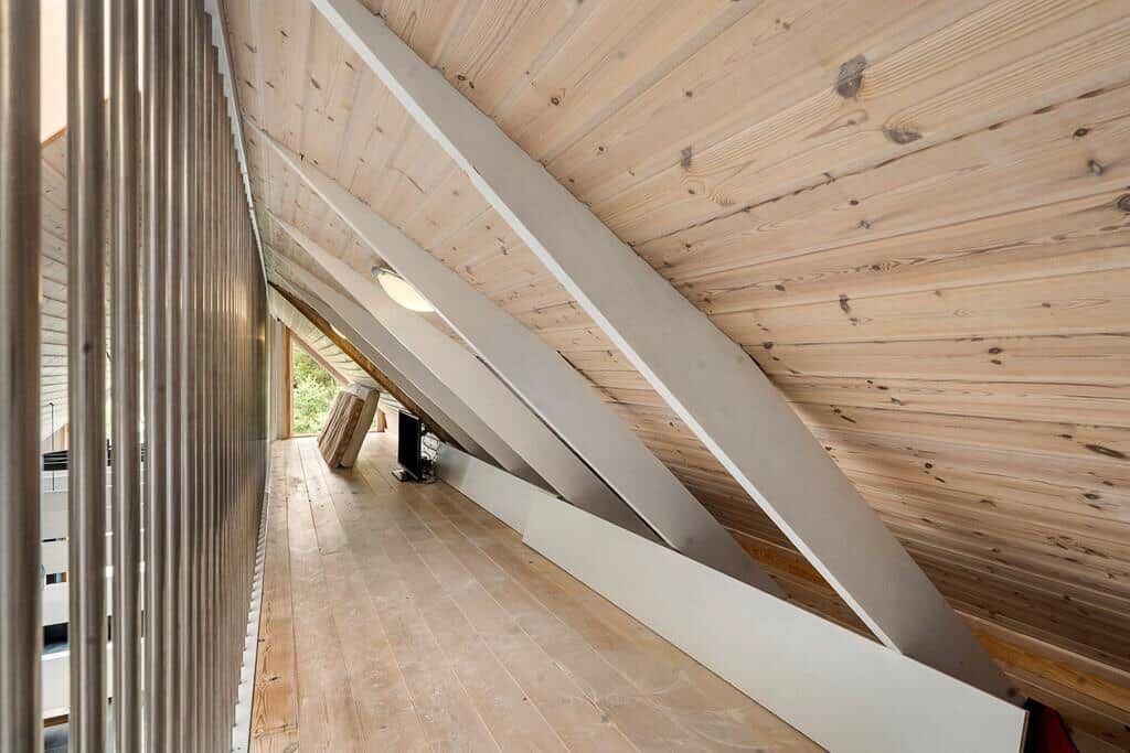 Dachgeschoss mit Holzdecke und weißen Trägern, Holzboden und Fensterblick nach draußen.