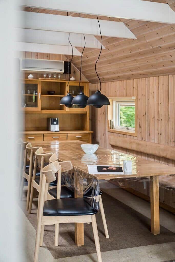 Esszimmer mit Holztisch, Stühlen und integriertem Küchenbereich unter Holzdecke.
