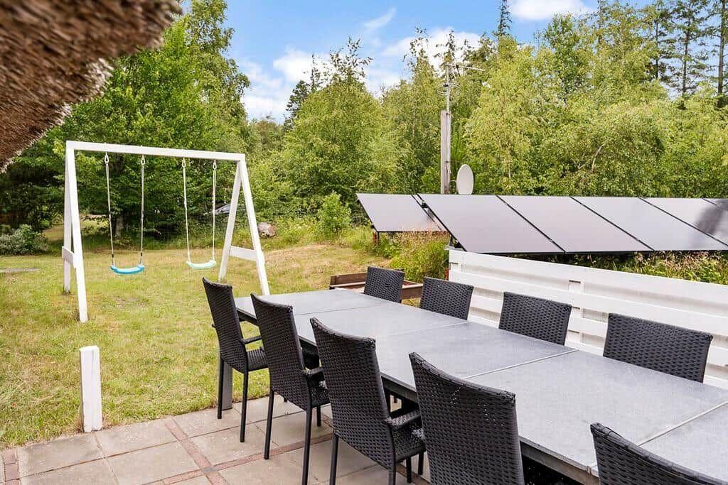 Außenbereich mit Tisch, Stühlen und Schaukel im Grün.