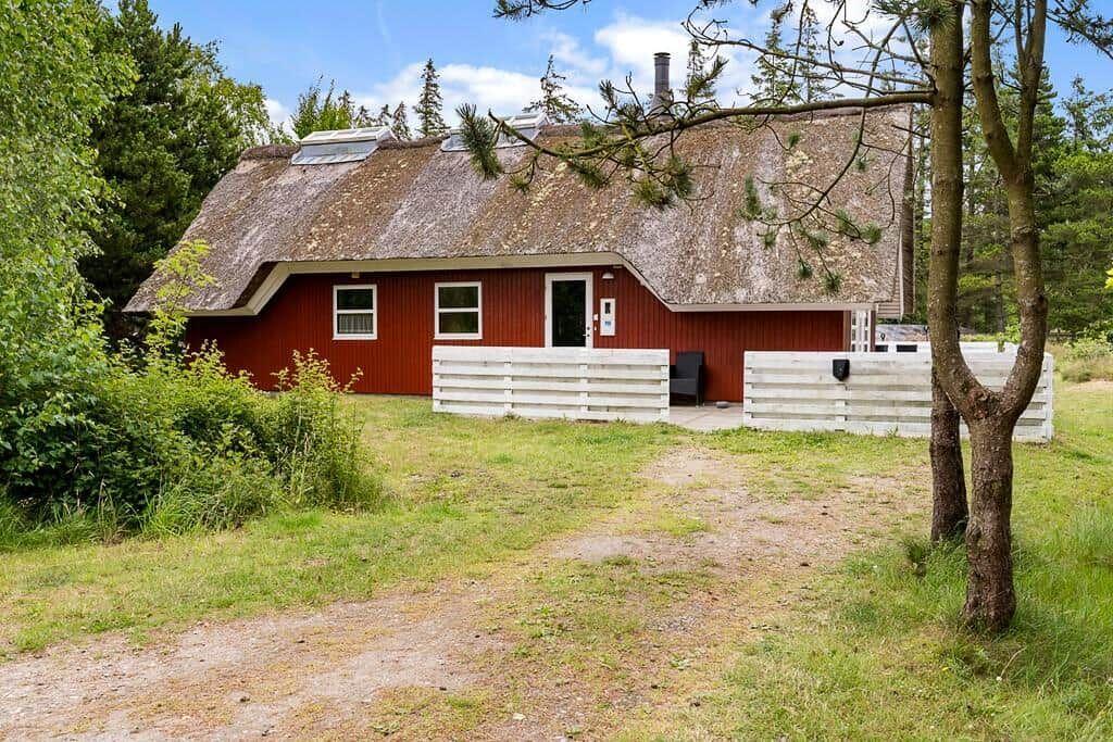 Rotes Holzhaus mit Strohdach, weißer Umzäunung und Gartenbereich.