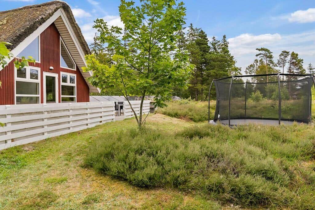Rotes Haus mit Strohdach, weißer Zaun und Trampolin im Garten.