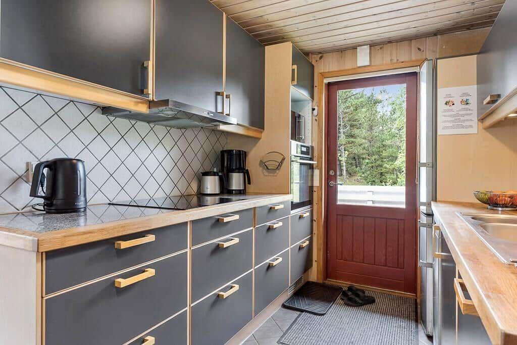 Küche mit dunklen Schränken, Holzoberflächen und Blick auf Balkon mit Wald.