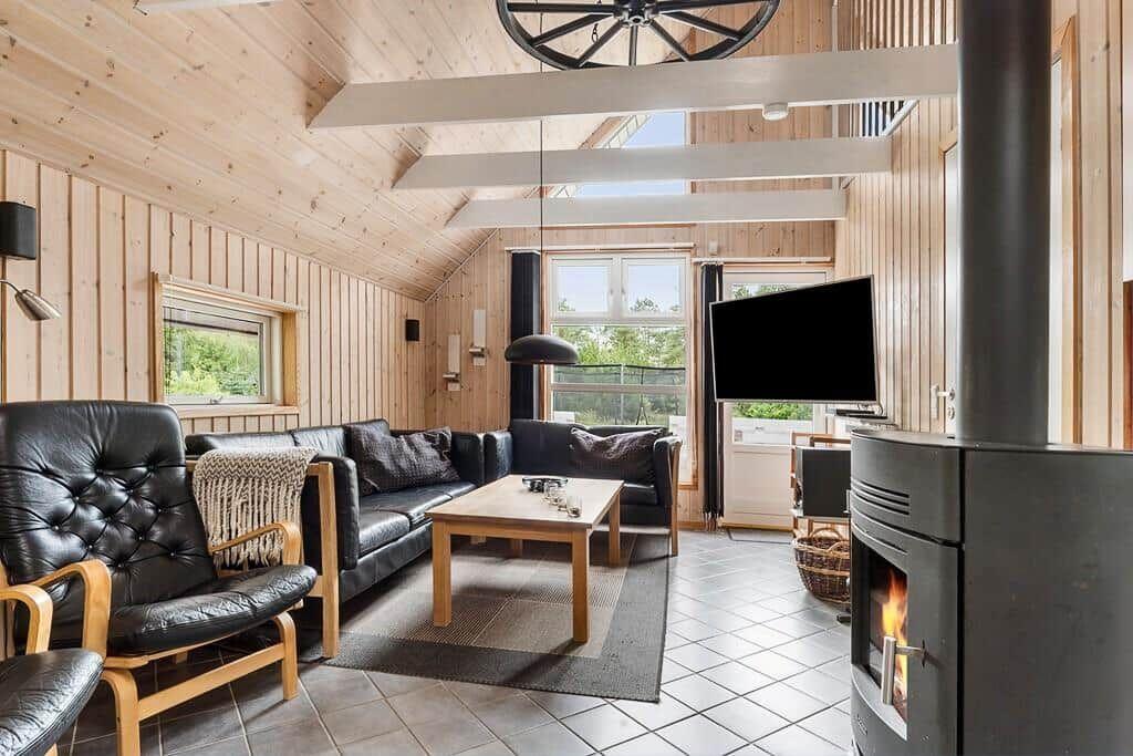 Wohnzimmer mit Holzwand, Sofa, Sessel, Kamin und TV.