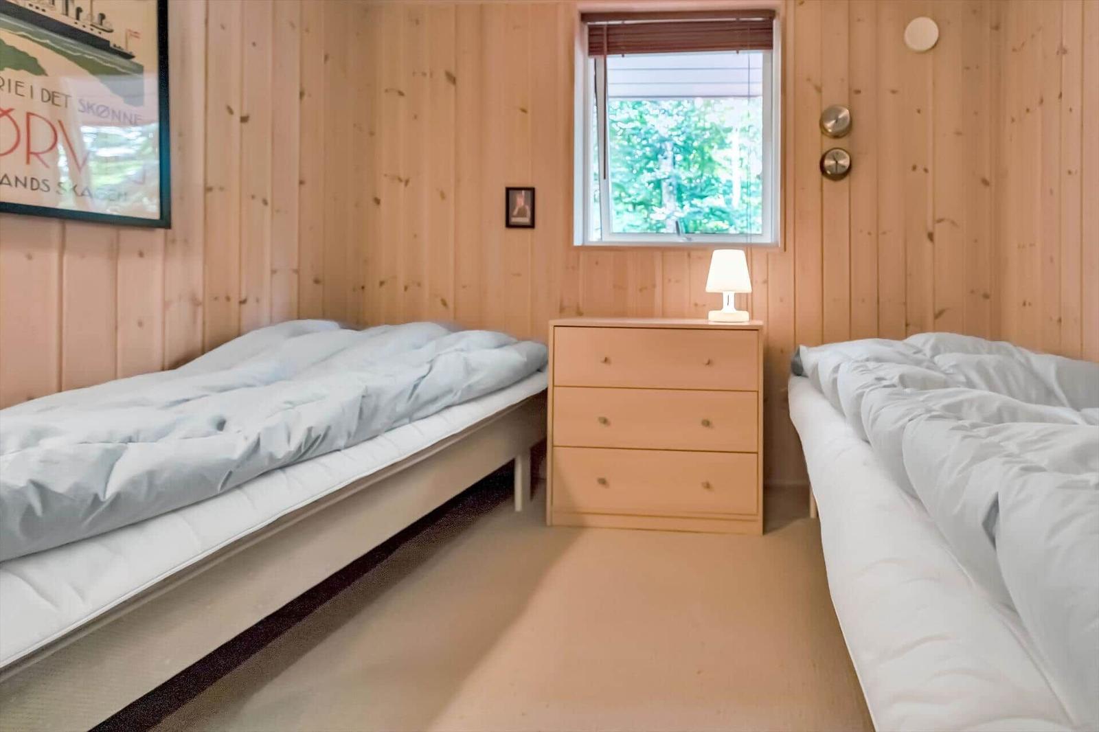 Zwei Betten, Nachttisch mit Lampe, Holzwand, Fenster mit Blick auf Grün.