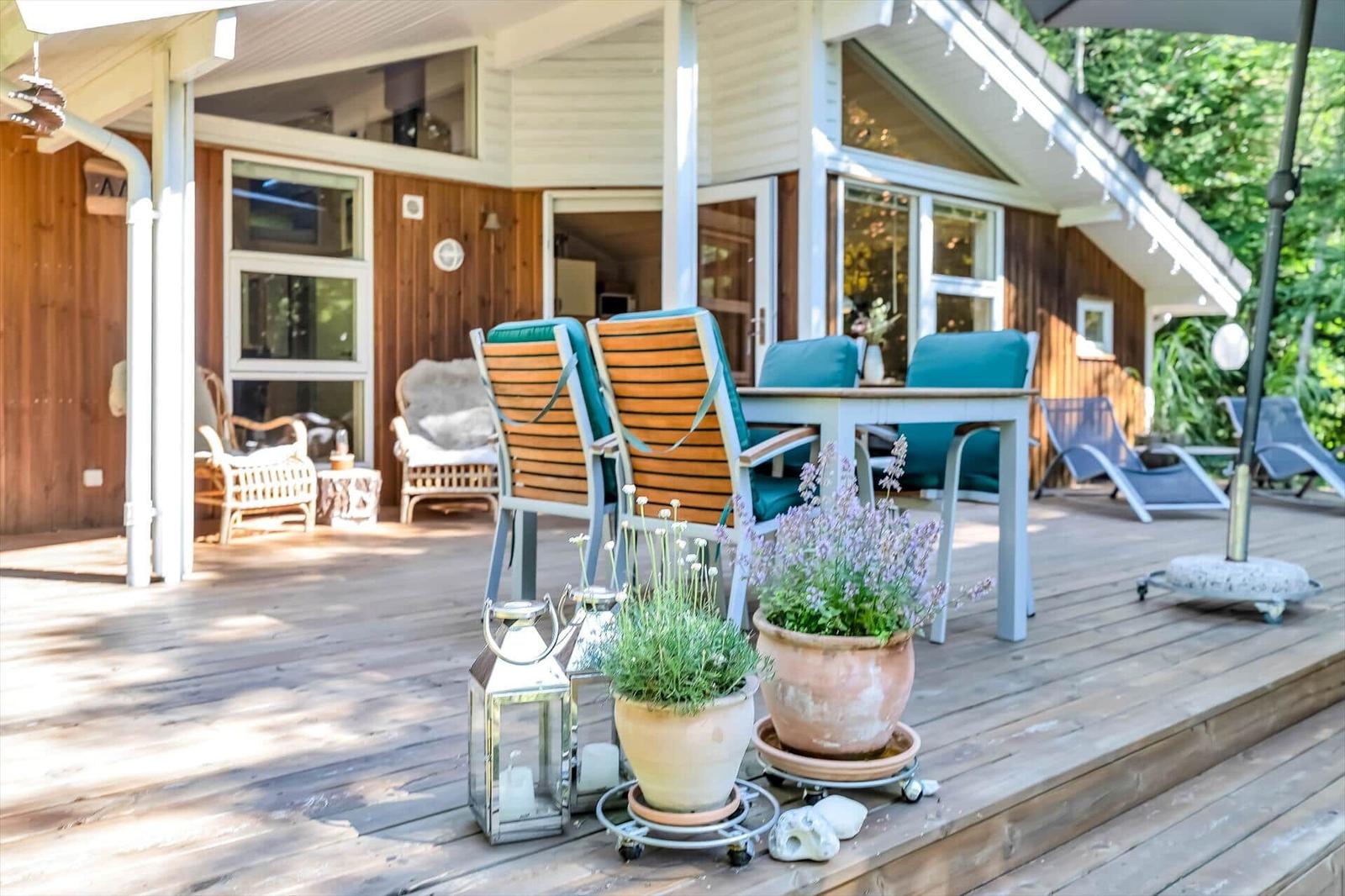 Terrasse mit Sitzgruppe, Pflanzen und Deckenliegen. Holzhaus mit großen Fenstern.