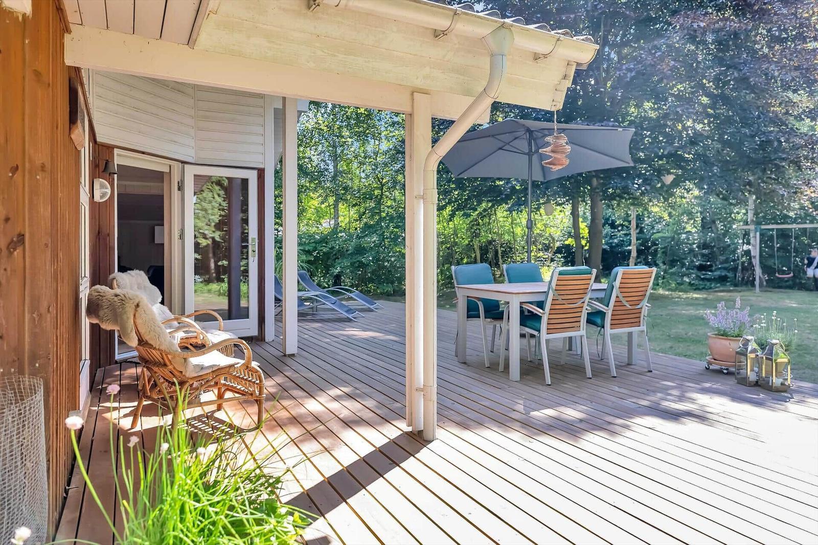 Terrasse mit Sitzgelegenheiten und Garten. Hintergrund: Wald und Schaukel.