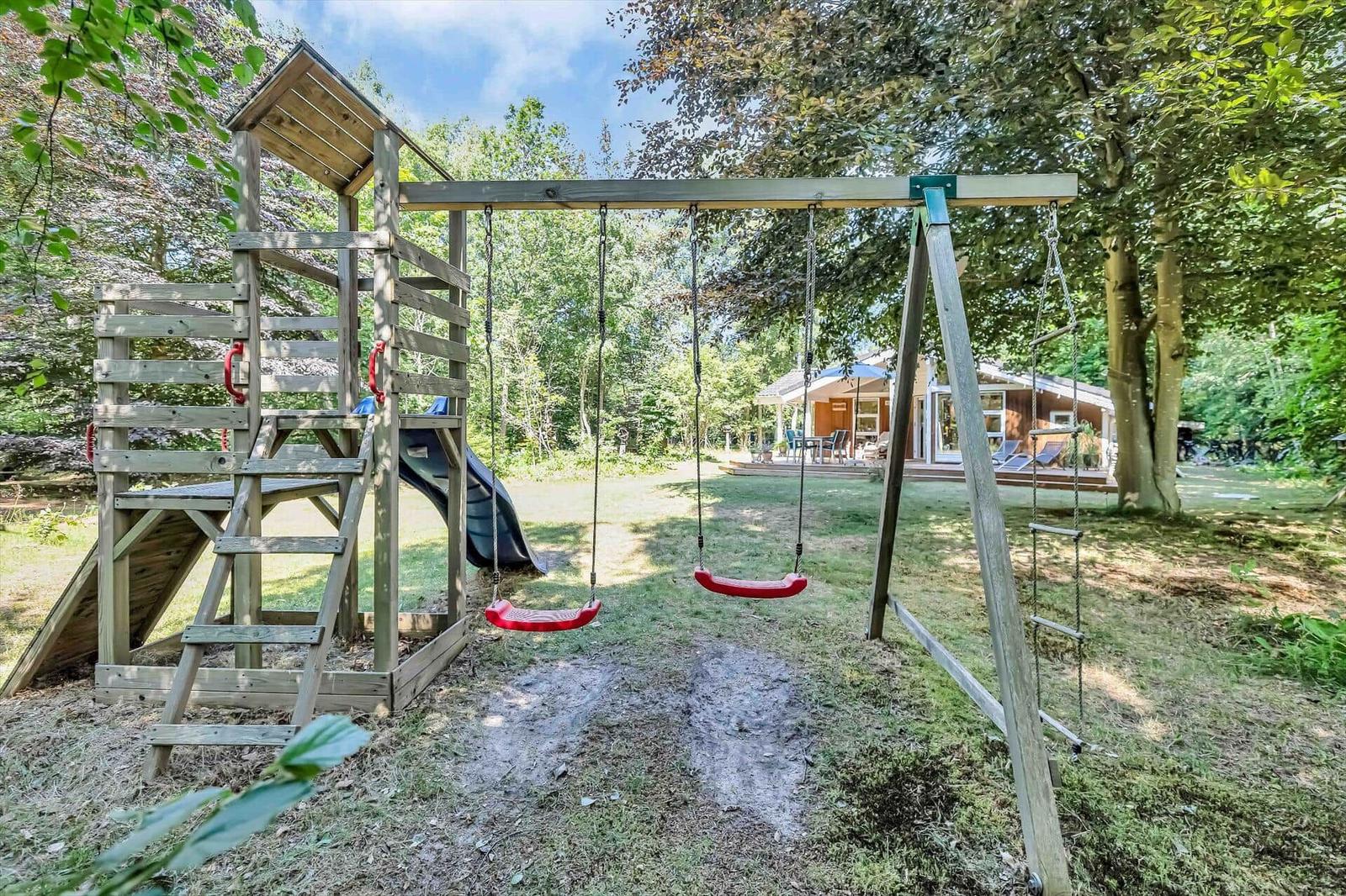 Holzspielplatz mit Rutsche und zwei roten Schaukeln im Garten.