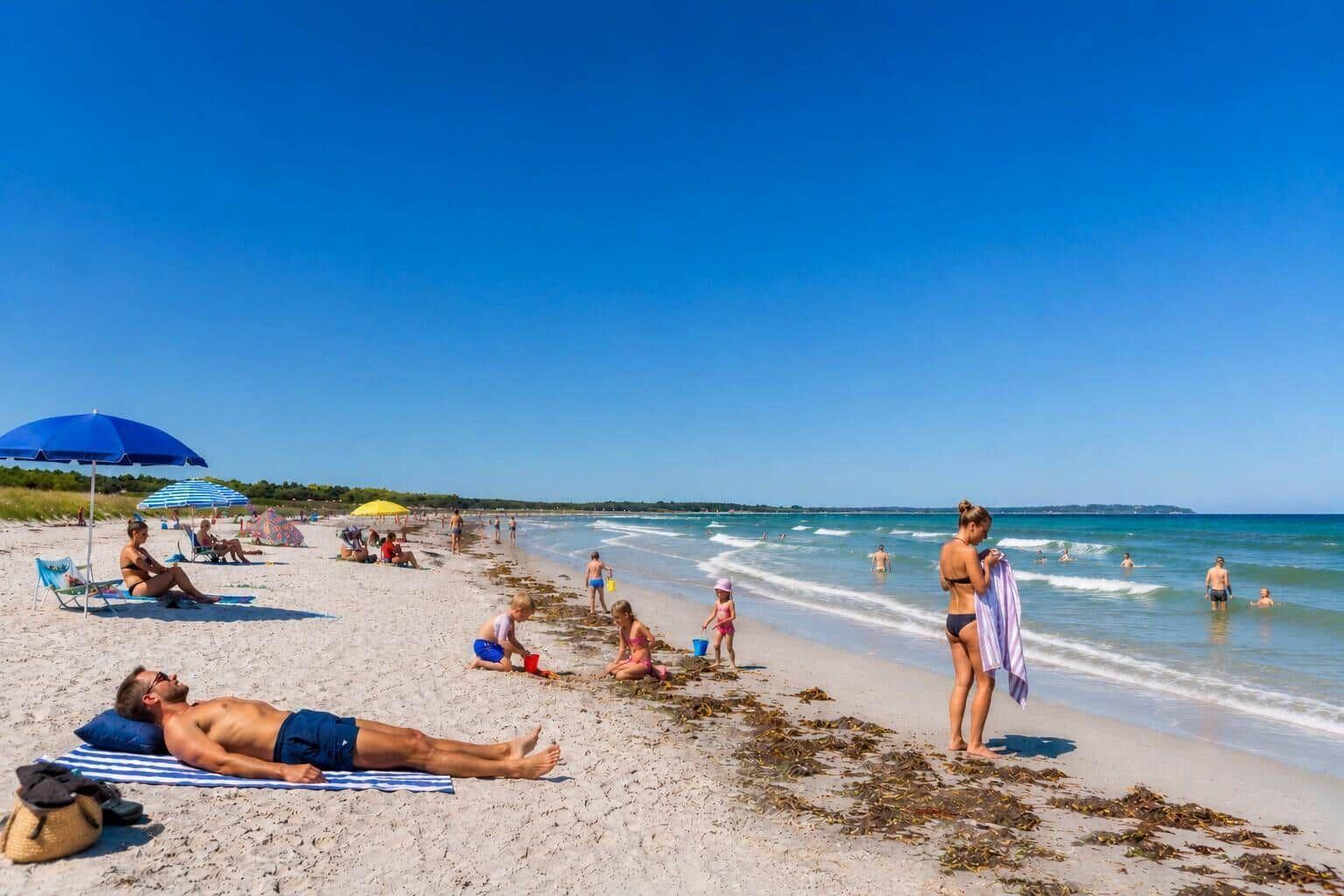 Strand mit Sonnenschirmen, Badegästen und Kindern, die im Sand spielen.