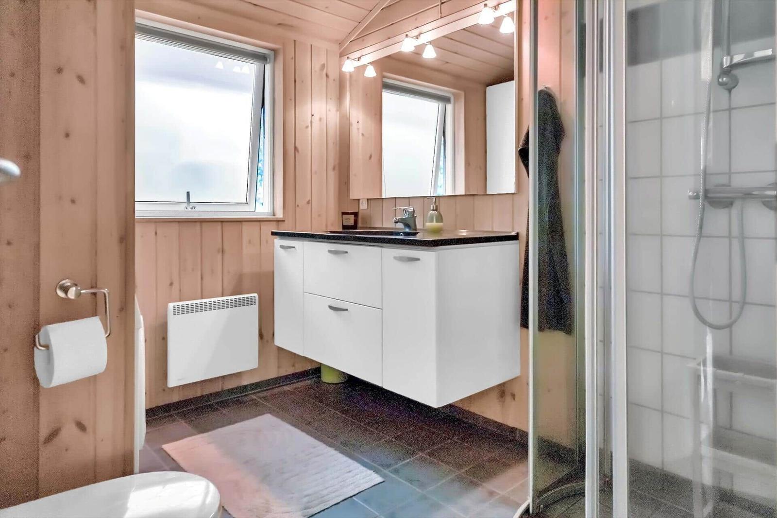 Badezimmer mit Dusche, Waschbecken und Fenster. Holzwände und Fliesenboden.