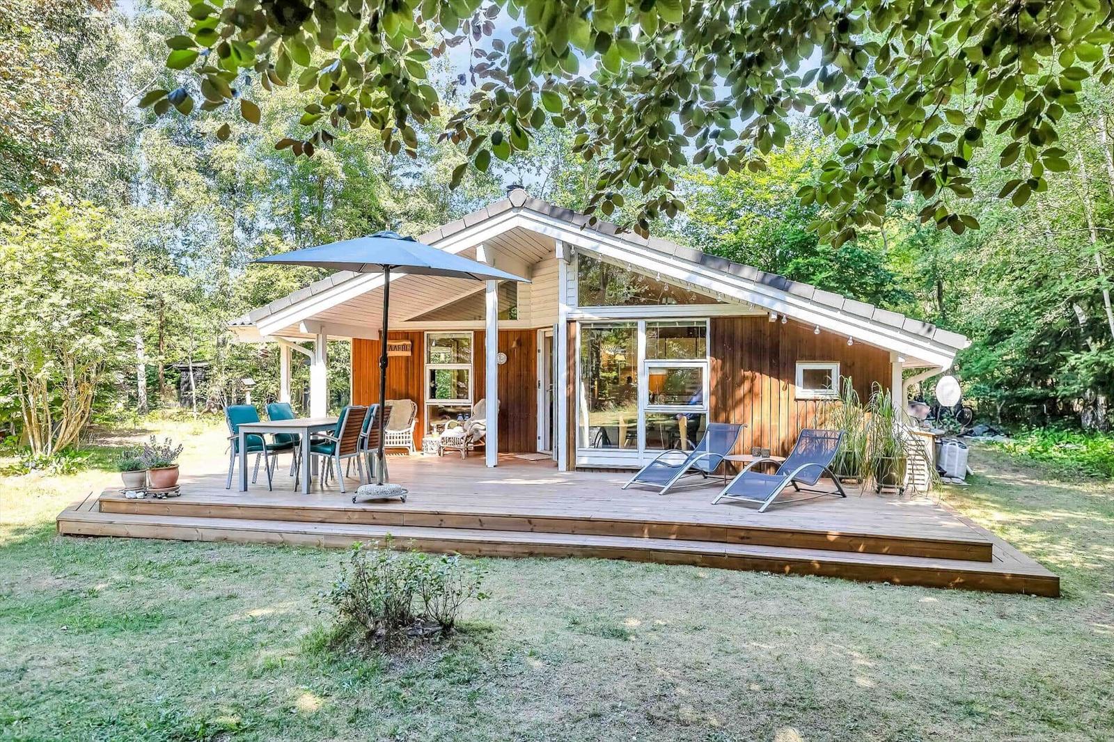 Holzhütte mit Terrasse, Sonnenliegen und Tisch unter einem Sonnenschirm im Wald.