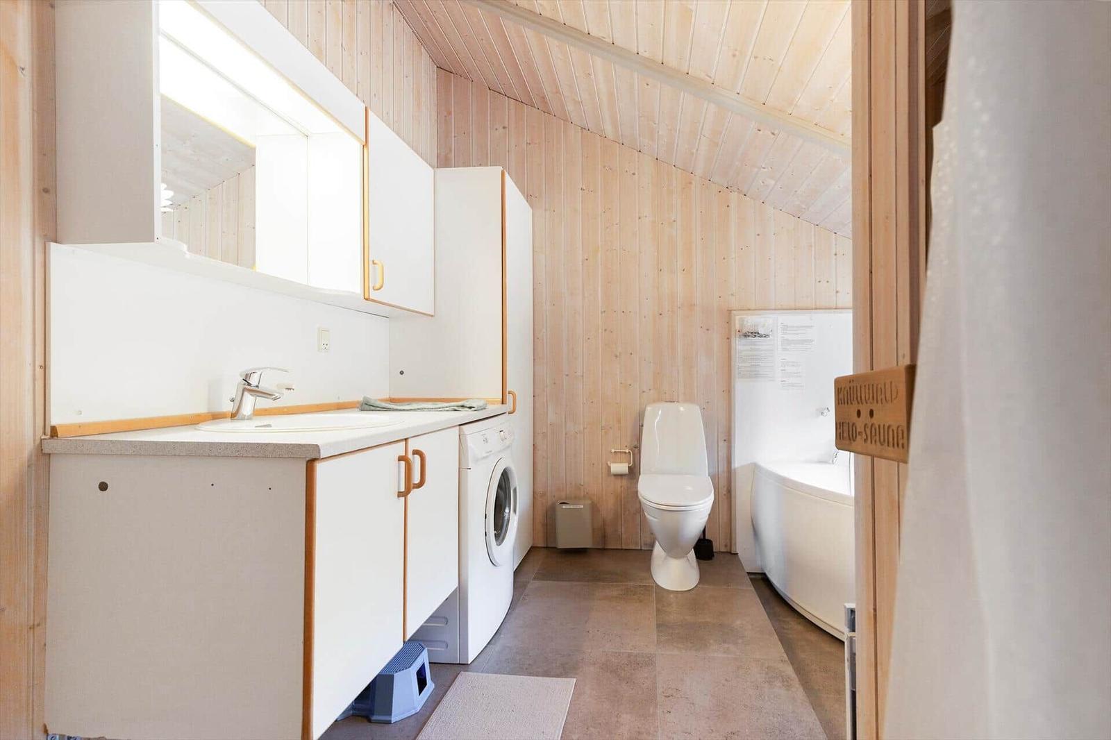 Badezimmer mit Waschmaschine, Toilette und Badewanne. Holzwände und -decke.