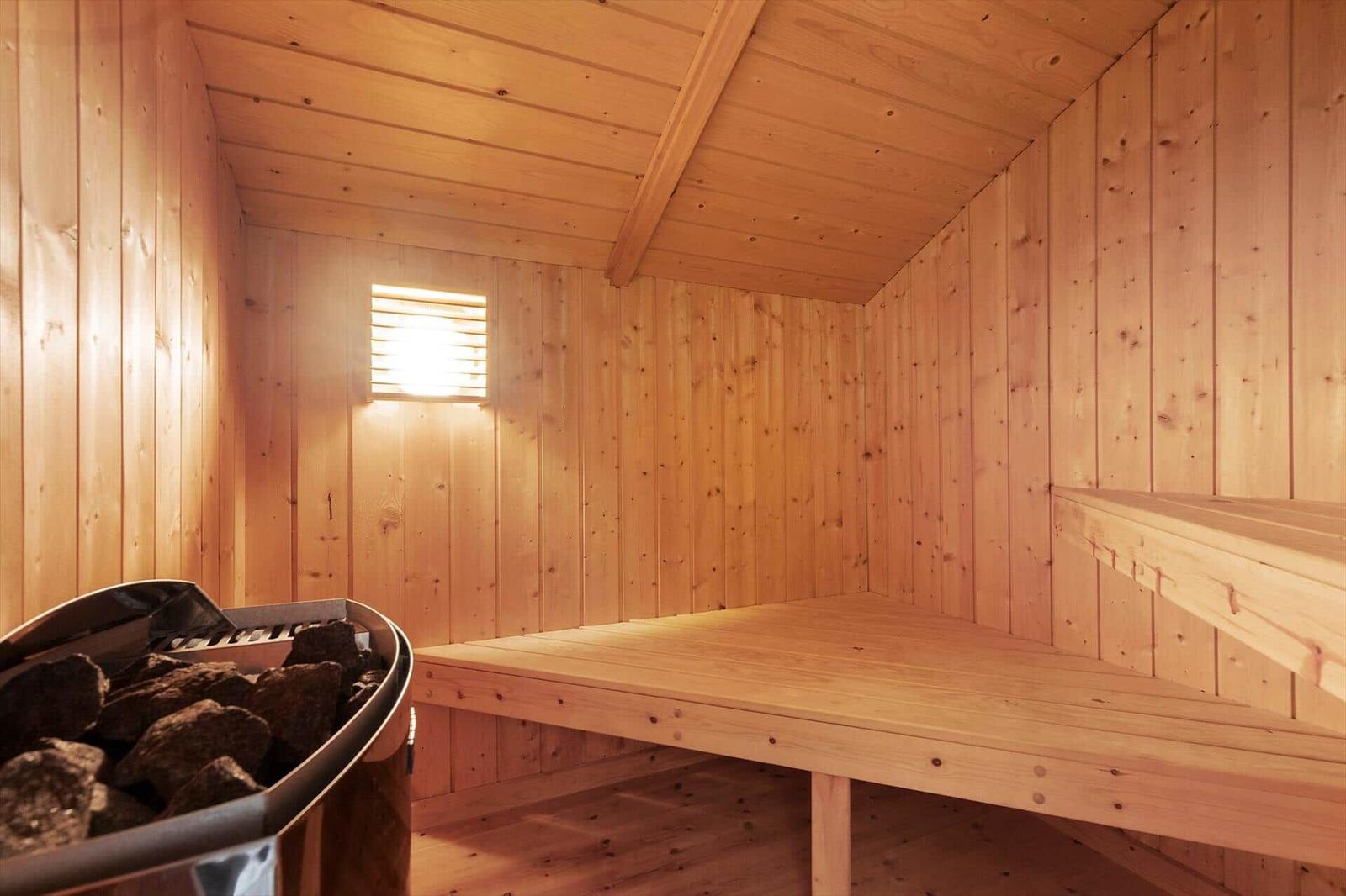 Sauna mit Holzwand, Sitzbank und Steinofen mit Steinen.