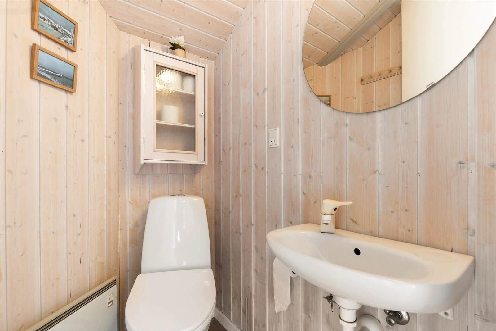 Bad mit Toilette, Waschbecken und Spiegelschrank an Holzwand.