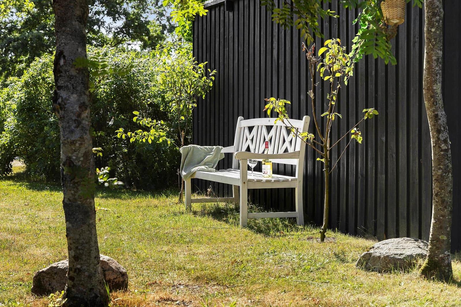 Weiße Bank mit Decke und Flasche vor schwarzem Holzhaus im Garten