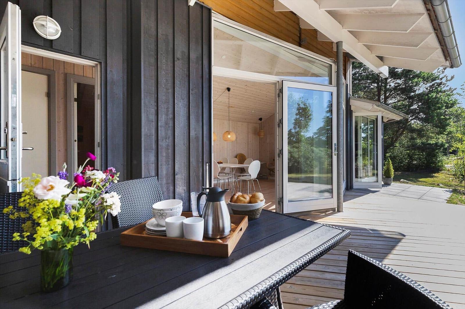 Terrasse mit Tisch, Stühlen und Blumen. Durchgehendes Glas führt ins Haus.