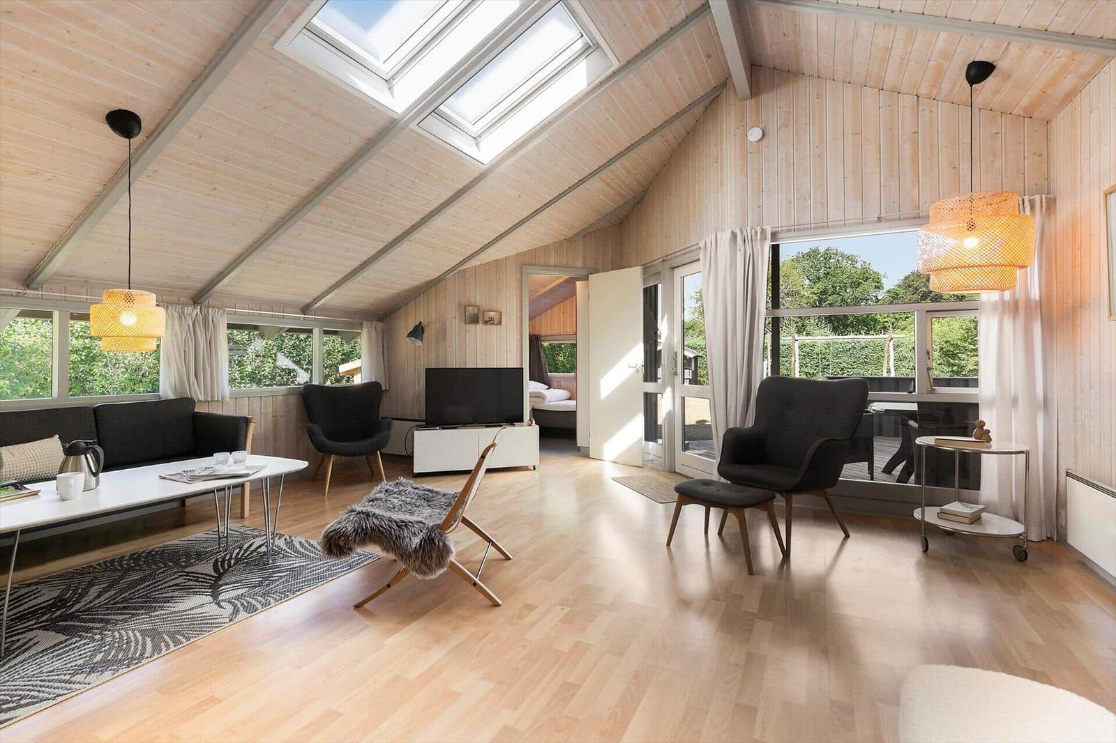 Wohnraum mit Holzdecke, großen Fenstern und moderner Einrichtung.